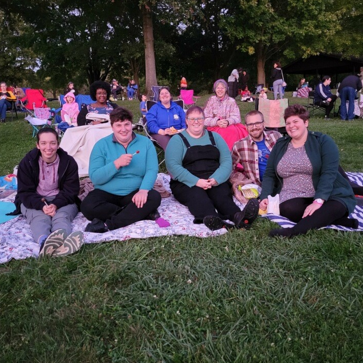 Smiling people sitting on a blanket in the park.